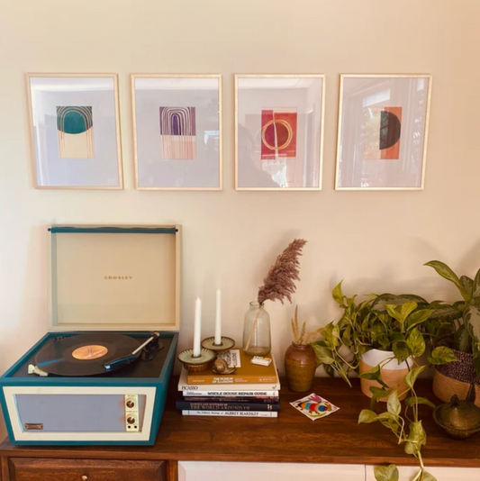 A retro record player beside plants and framed abstract art on a wall.