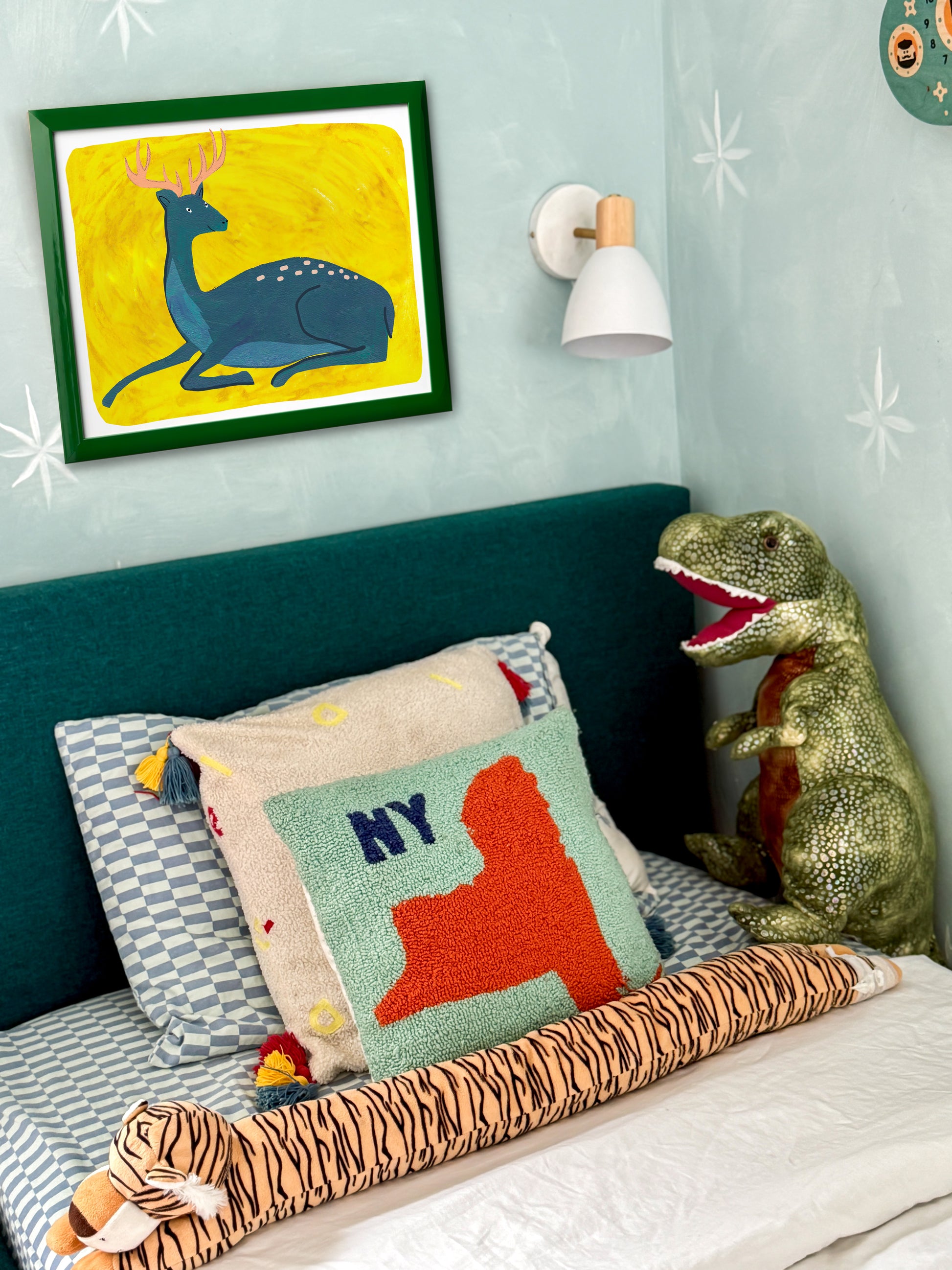 Cozy bedroom corner with a blue deer painting, a green headboard, decorative pillows, and stuffed animal toys.