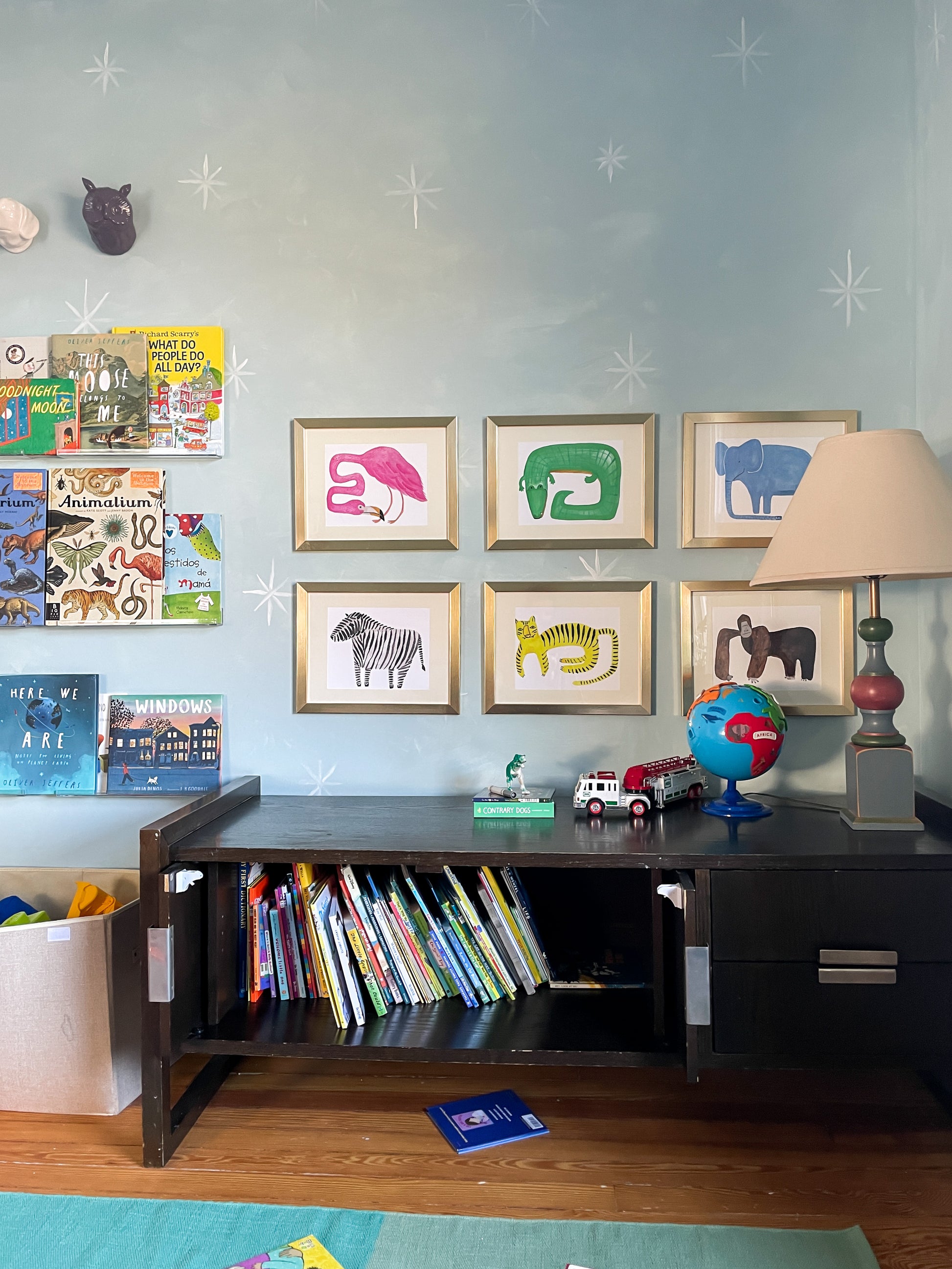 A colorful children's room featuring framed animal art, a bookshelf filled with books, a lamp, and a globe.