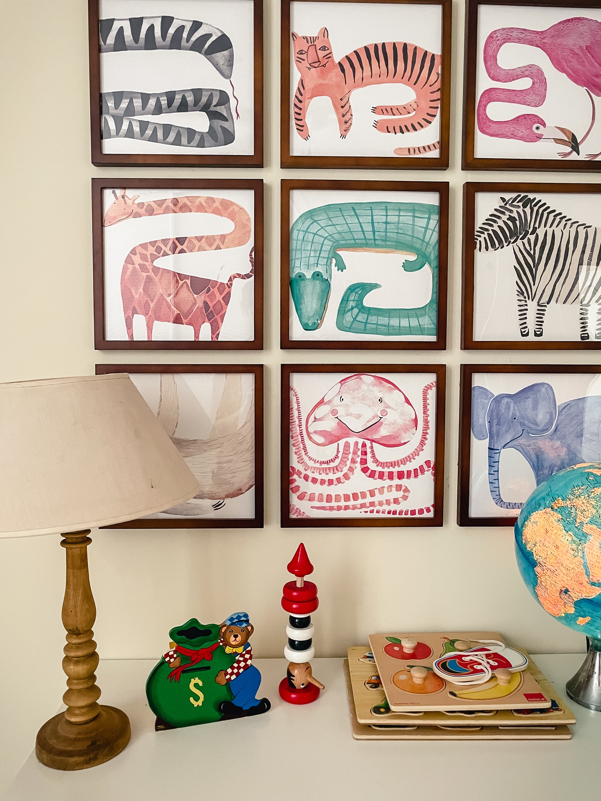 A decorative wall with colorful animal illustrations, a lamp, a globe, and vintage toys on a table.