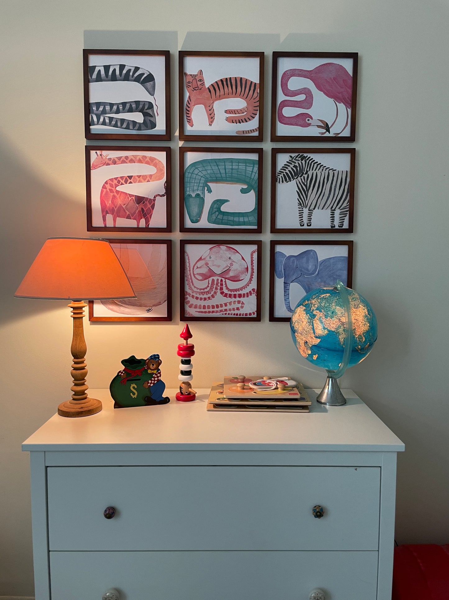 A cozy room featuring a dresser with a lamp, a globe, and children's animal artwork on the wall.