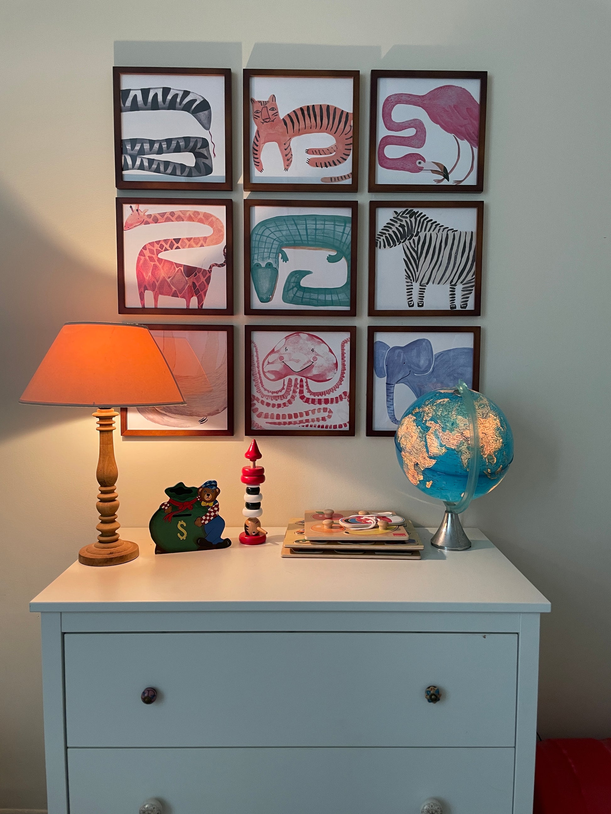 A cozy room featuring a dresser with a lamp, a globe, and children's animal artwork on the wall.