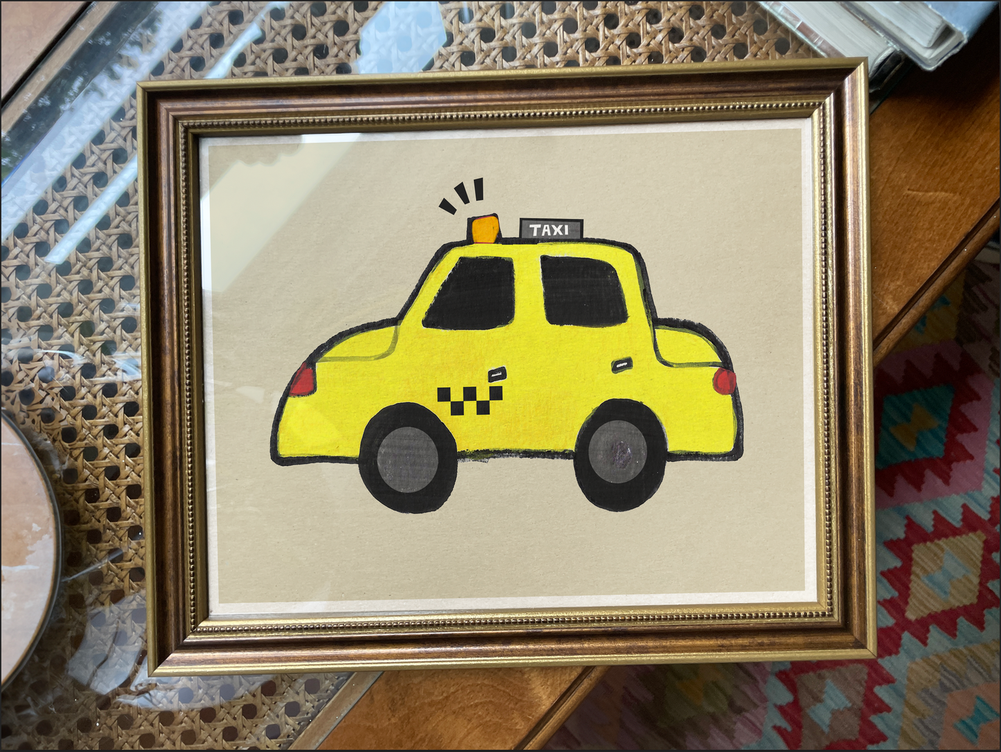 A framed drawing of a yellow taxi cab on a beige background.
