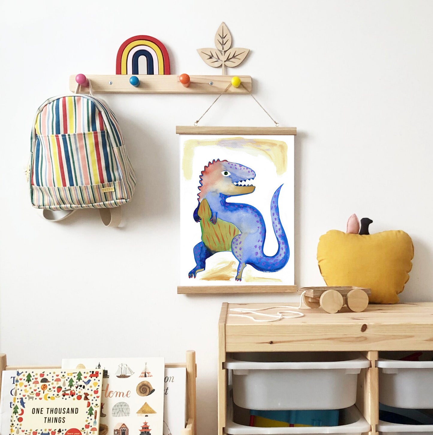 Colorful dinosaur illustration hanging on a wall with a striped backpack and a plush toy.
