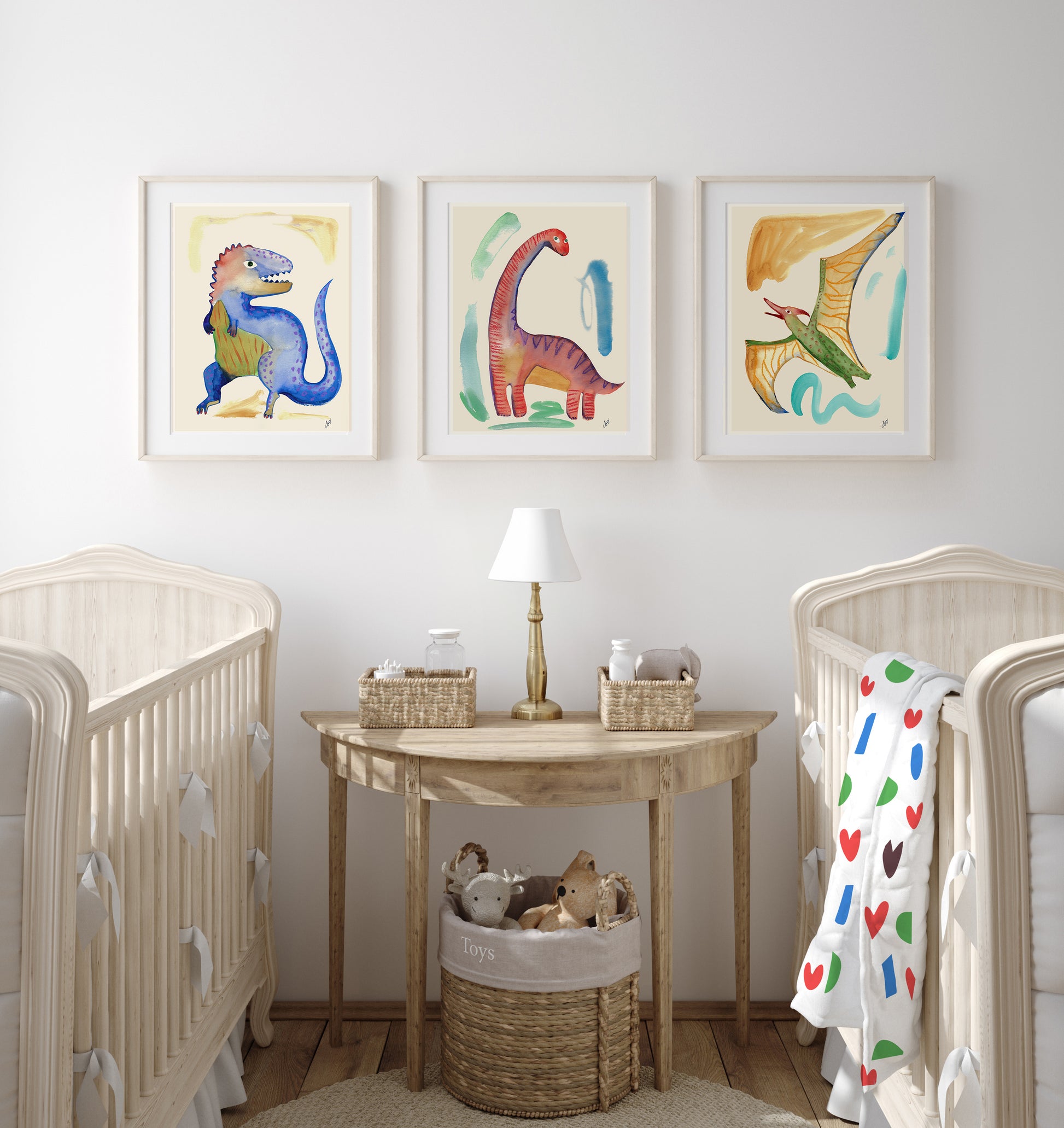A nursery featuring two cribs, a decorative table with a lamp, and colorful dinosaur artwork on the walls.