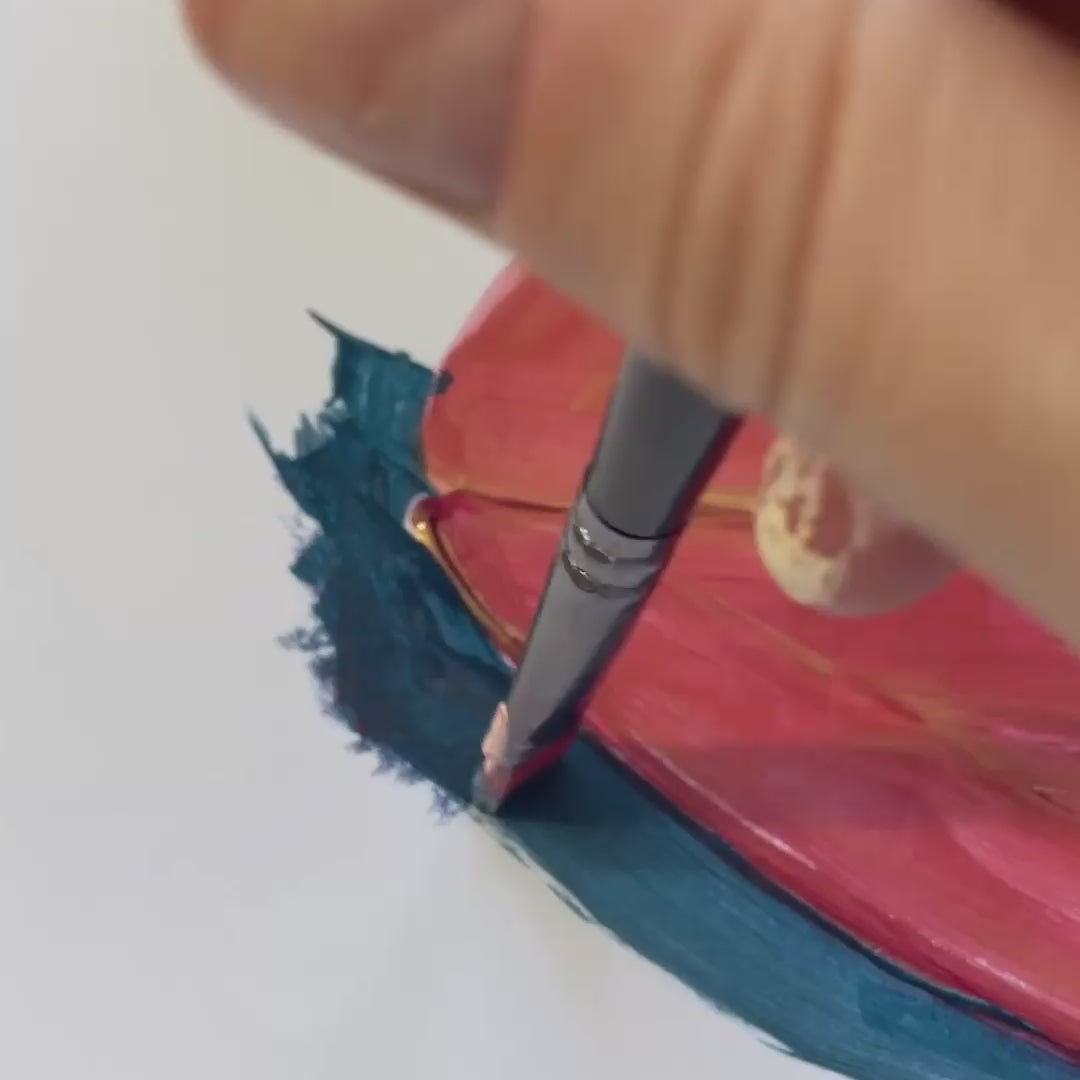 A close-up of a hand holding a paintbrush, applying blue paint to a vibrant pink surface.