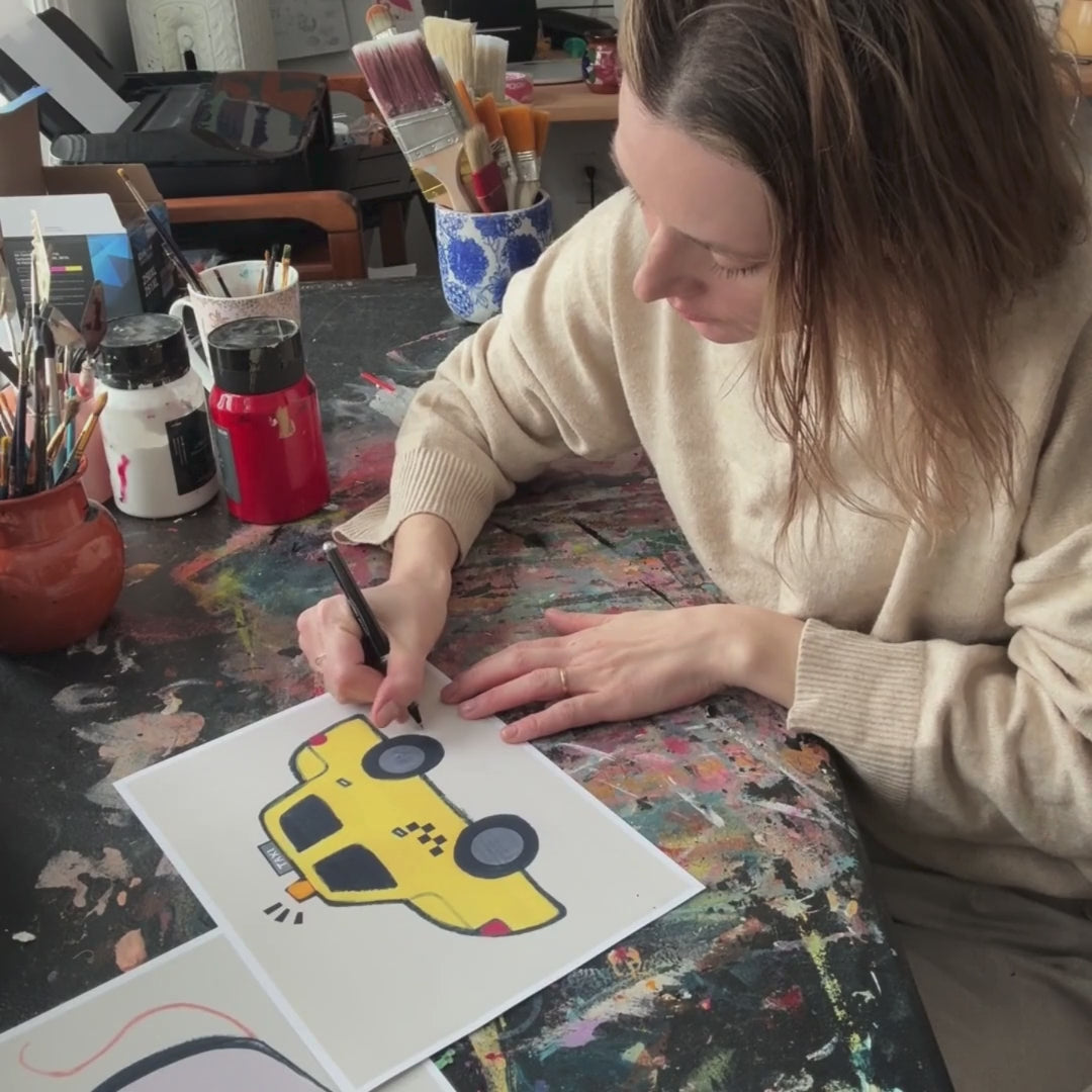 Person drawing a cartoon yellow car on paper at an art table.