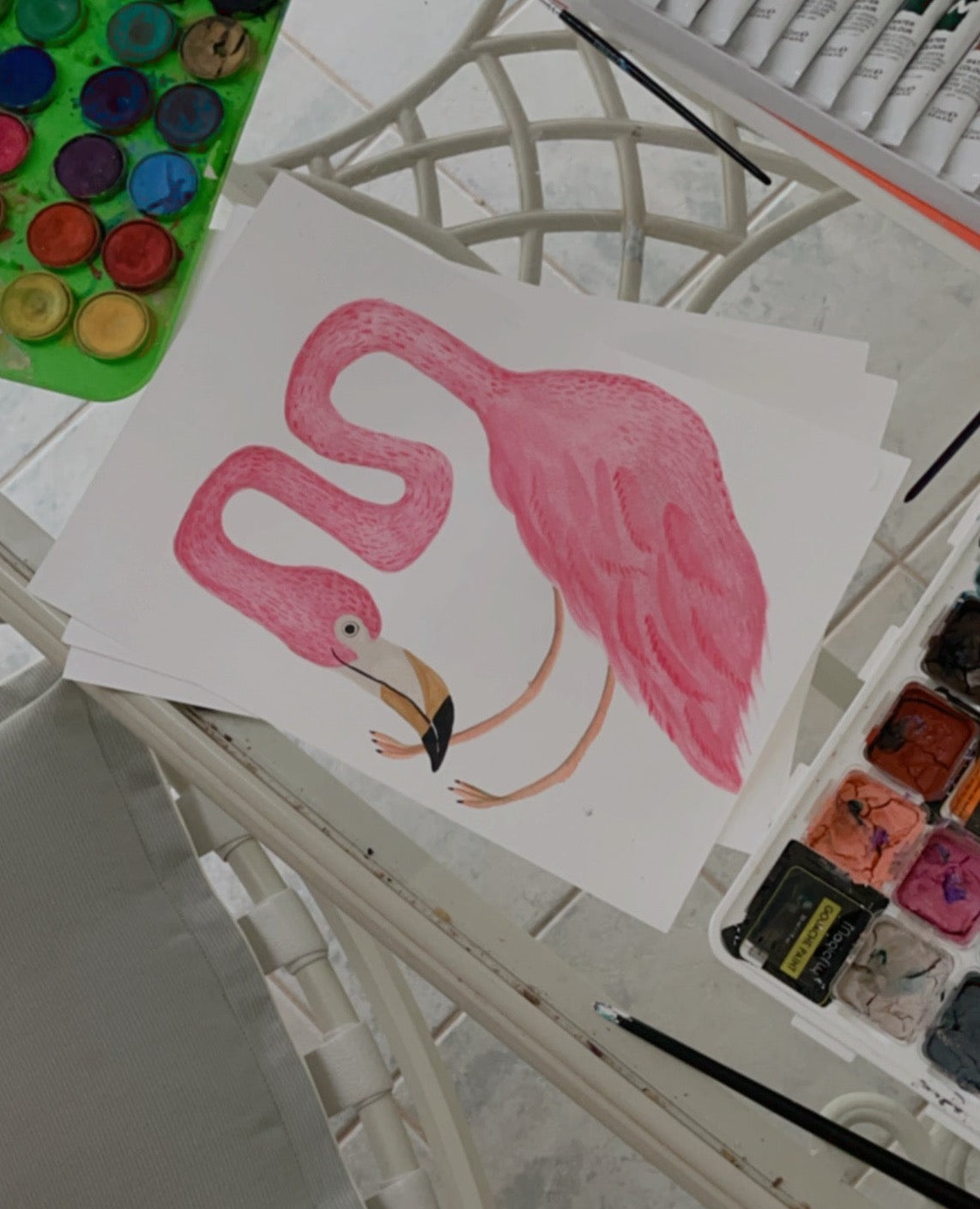 A colorful illustration of two pink flamingos on a table with art supplies.