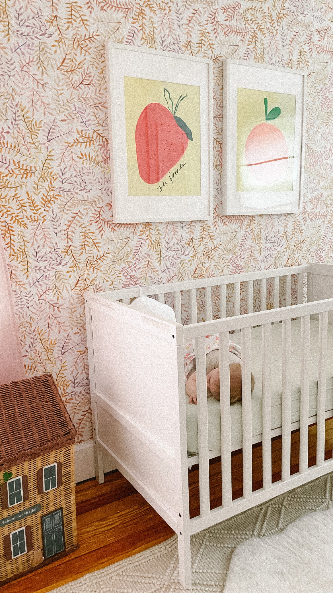A cozy nursery featuring a white crib, colorful fruit-themed artwork, and a decorative toy house.