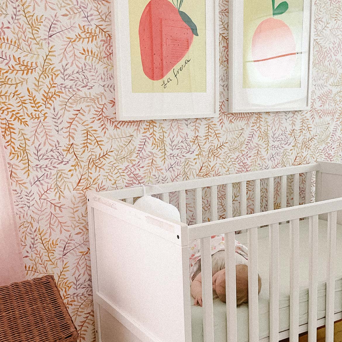 A cozy nursery with a white crib, leafy wallpaper, and fruit-themed artwork.