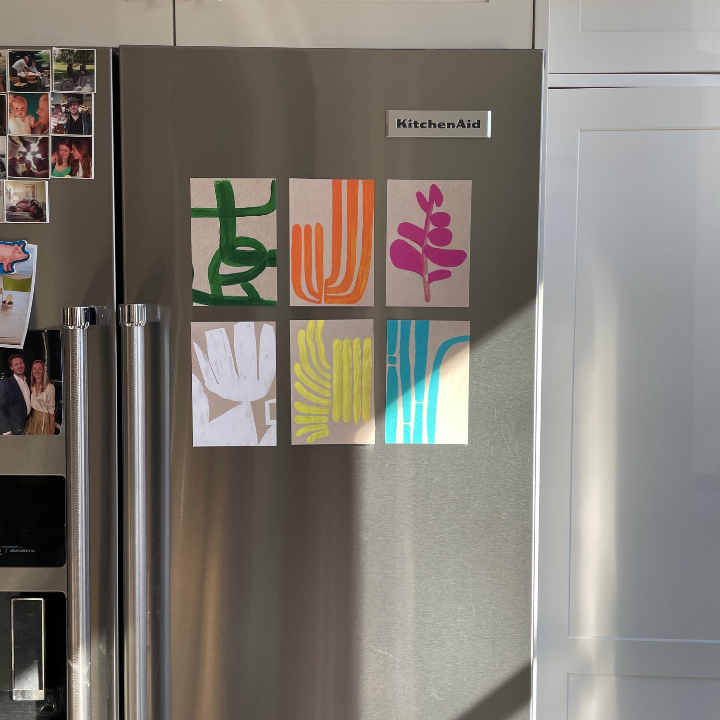 Colorful abstract art pieces displayed on a refrigerator door.