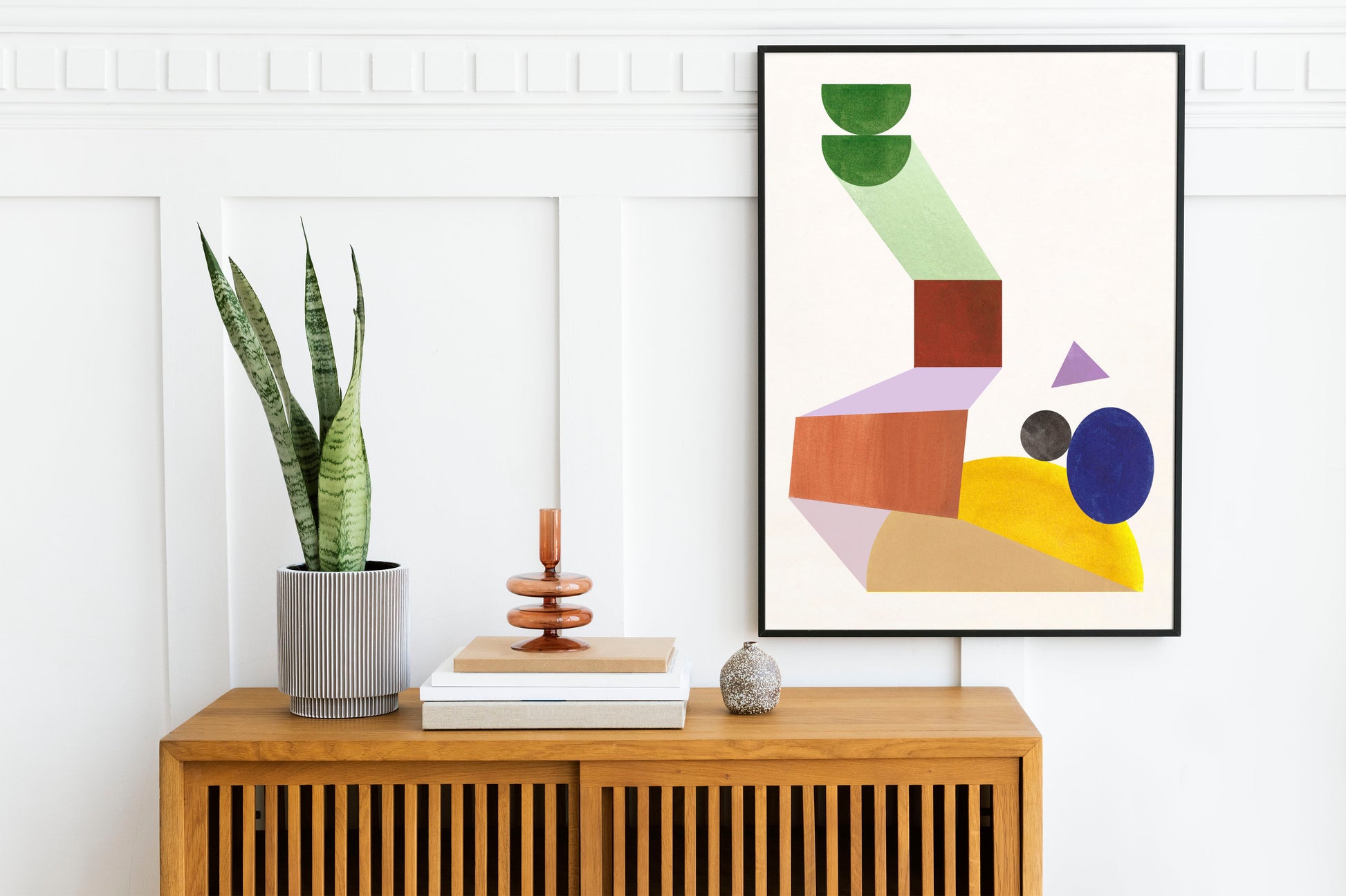 A modern interior scene featuring a framed abstract artwork above a wooden sideboard with a potted plant and decorative items.