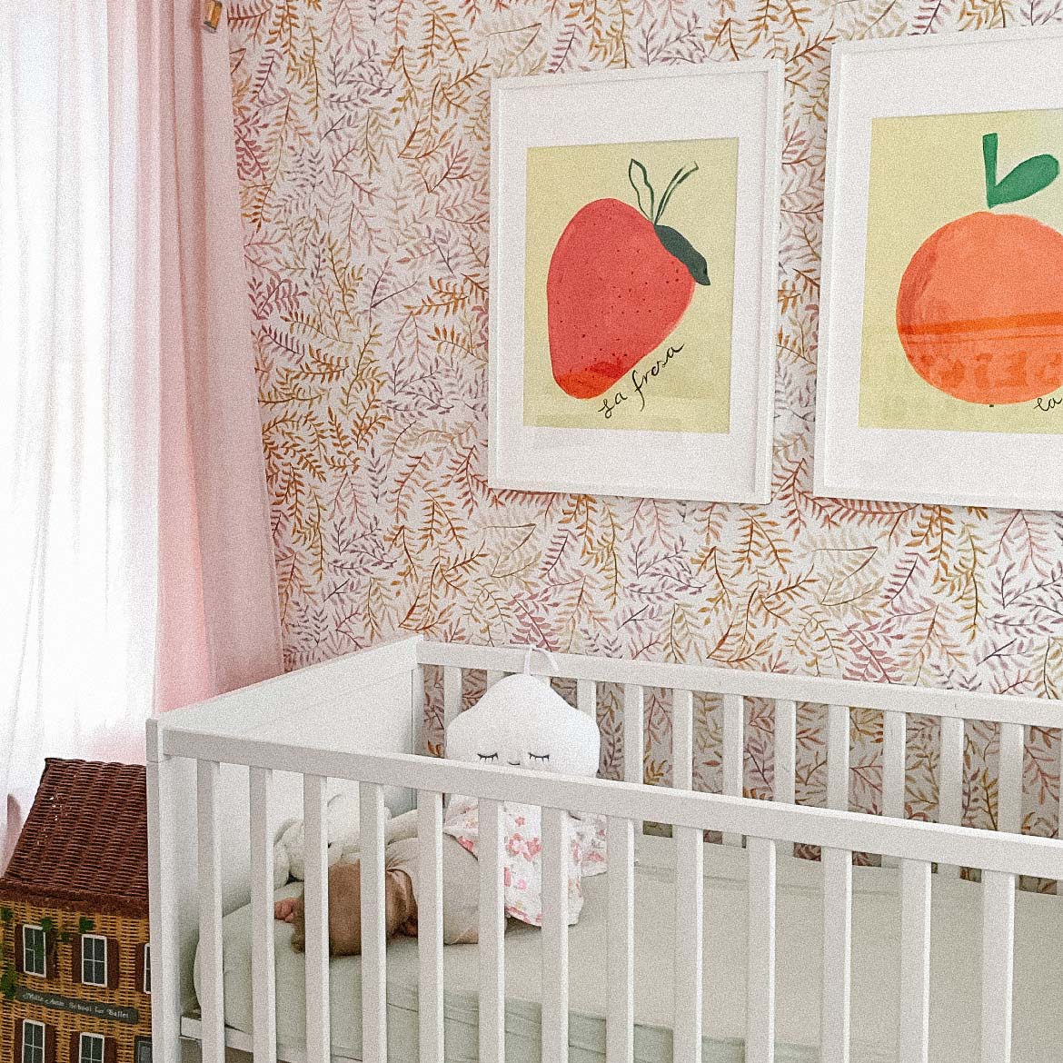 A cozy nursery featuring a white crib, colorful fruit-themed artwork on the walls, and soft pastel decor.