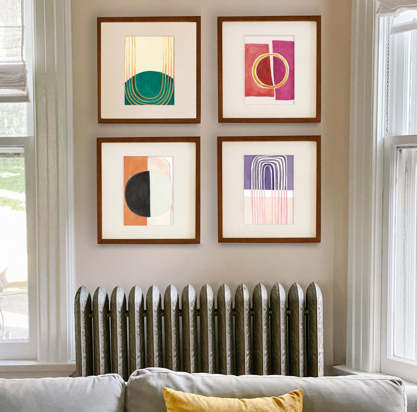 Four framed abstract art pieces on a wall above a radiator, with a cozy sofa in the foreground.